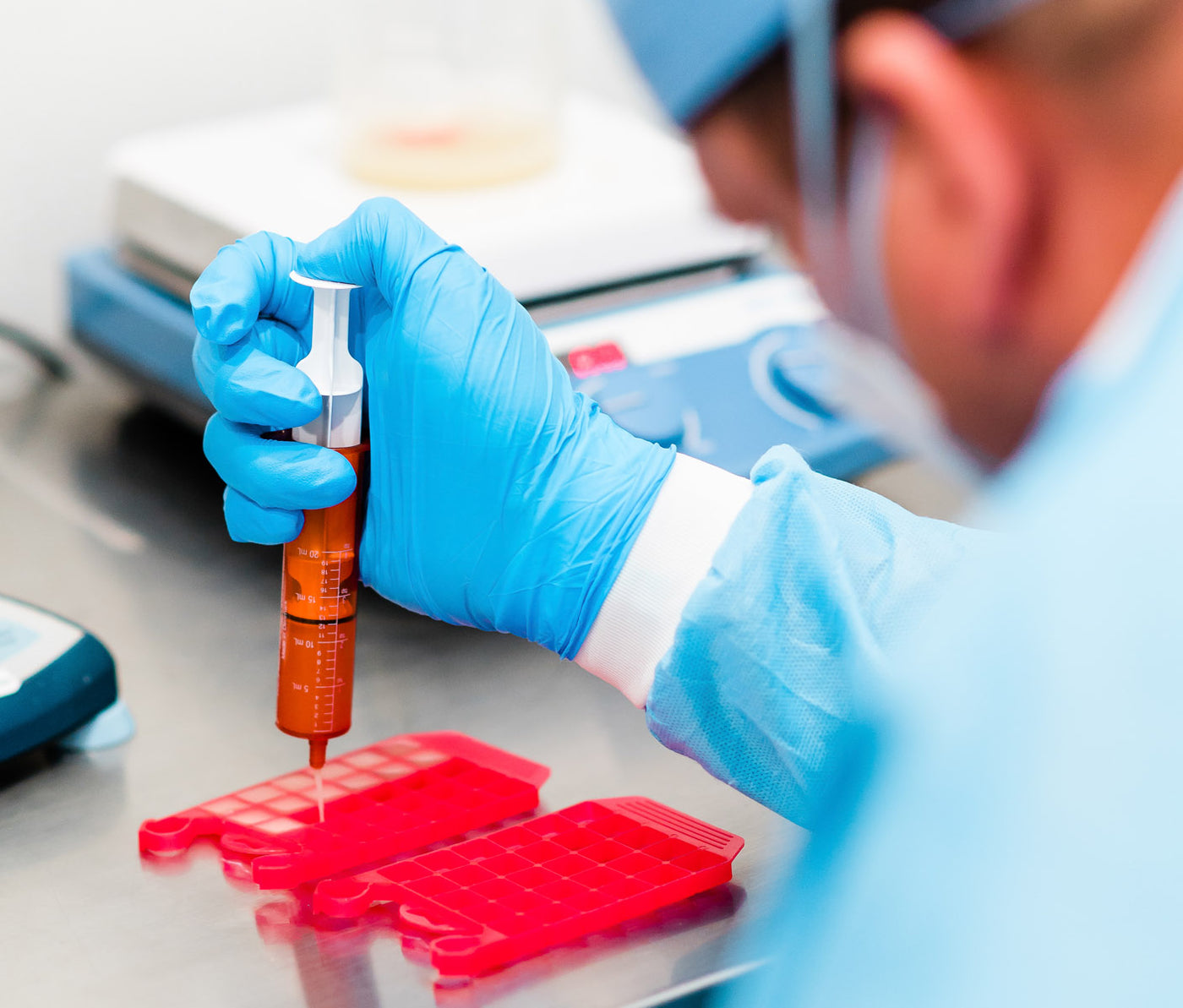 Compounding pharmacist in protective gear using a needleless syringe to fill a troche mold tray at Thornhill's Pharmacy